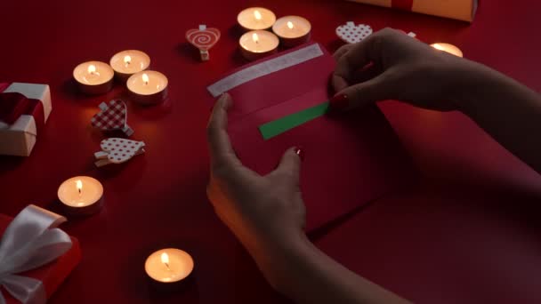 Kobiety otwierają kopertę i wyjmują walentynkową kartę z zielonym kluczem chromowym. Widok z góry czerwony stół z płonącymi świecami, dekoracyjne serca i prezent. Romantyczny zmierzch. Zamknij drzwi. Zwolniony ruch — Wideo stockowe