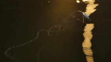 Terk edilmiş bir pusula sarı ışıklı suda yüzer. Karanlık bir stüdyoda, parlak suyun yüzeyine yağmur damlaları düşer. Kapatın. Yavaş çekim.