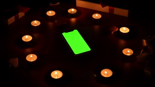 Top view of smartphone with green screen chroma key on red table in center burning candles, hearts, valentine and gift. Romantic twilight background with lights. Valentines Day. Close up. Slow motion — Stok video