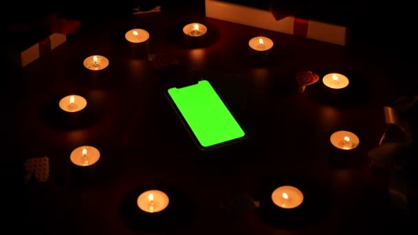 Top view of smartphone with green screen chroma key on red table in center burning candles, hearts, valentine and gift. Romantic twilight background with lights. Valentines Day. Close up. Slow motion — Vídeo de stock