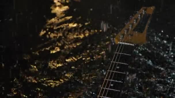Raindrops fall on the electric guitar and drum on the strings. The strings of a musical instrument tremble and create fine splashes. Dark studio with yellow lighting. Close up. Slow motion. — Stock Video