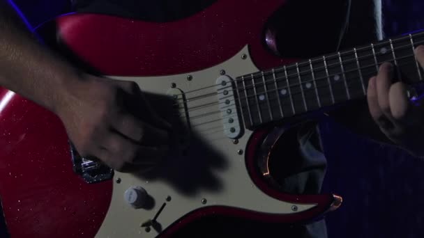 Rock zenész játszik egy piros fehér elektromos gitár egy sötét stúdióban hátterében eső csepp. Közelről férfi kezek játszanak húrok gitár csákány. Lassú mozgás.. — Stock videók
