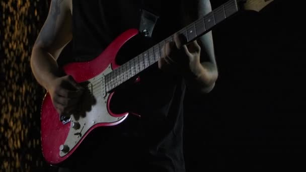 Rock muzikant speelt een rood witte elektrische gitaar in een donkere studio tegen de achtergrond van vallende regendruppels. Close-up van de mannelijke handen spelen op snaren met gitaar pick. Langzame beweging. — Stockvideo