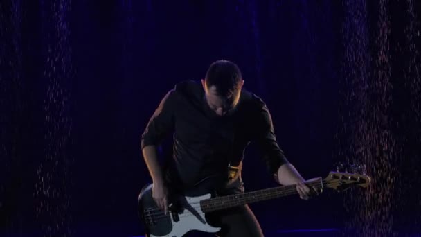 Musicista rock barbuto magistralmente suona solo al basso in uno studio buio con luci blu. Il chitarrista si esibisce dal vivo sotto la pioggia battente. Chiudete. Rallentatore. — Video Stock