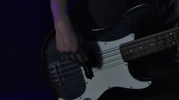 Rock musician plays a black white bass guitar in a dark studio against the background of falling rain drops. Close up of male hands play on strings. Slow motion. — Wideo stockowe