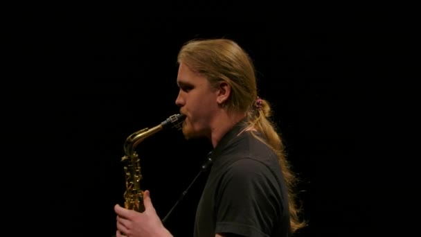 Kamera se točí kolem mladíka hrajícího na saxofon. Hudebník izolovaný na černém pozadí v tmavém studiu. Zavřít. Zpomalený pohyb. — Stock video