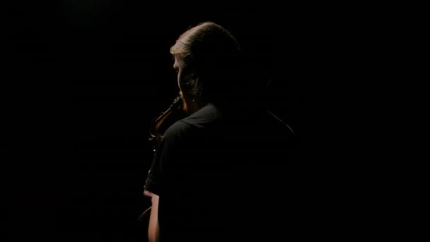 Orbitális felvétel egy szaxofonosról, aki arany szélhangszeren játszik a sötétben. Fiatal férfi, fekete háttérrel, műtermi fénnyel megvilágítva. Közelről. Lassú mozgás..