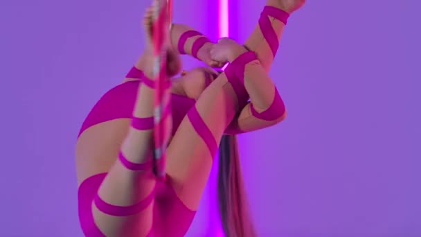 Aerial acrobat in the ring. A young girl in a pink leotard performs acrobatic elements on the air hoop. Shot in the studio with bright neon lights in the background. Close up. Slow motion. — Stock Video