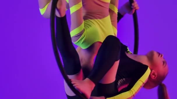 Due giovani ragazze eseguono elementi acrobatici su un cerchio pneumatico. Acrobati aerei in uno spettacolo circense sullo sfondo di luci al neon luminose. Chiudete. Rallentatore. — Video Stock