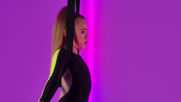 Young girl acrobat rotates in an air hoop and performs tricks while walking through air. A circus performer in black leotard performs against the backdrop of bright neon lights. Close up. Slow motion. — Stock Video