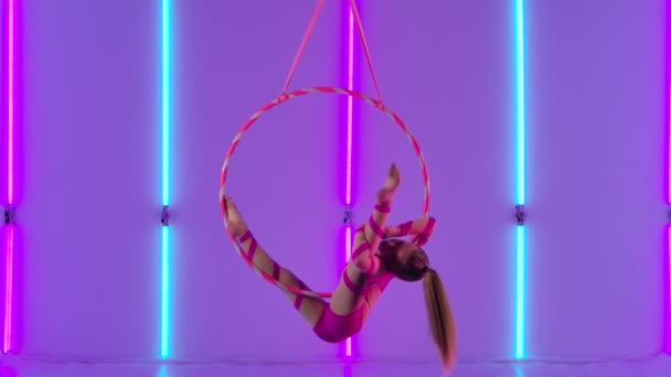 Vzdušný akrobat v ringu. Mladá dívka v růžovém trikotu předvádí akrobatické prvky na vzduchovém koši. Natočeno ve studiu s jasnými neonovými světly v pozadí. Zpomalený pohyb. — Stock video