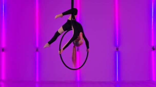 Flexibilní mladý gymnastka visí hlavou dolů na vzduchovém koši a provádí akrobatické prvky. Dívka v černém trikotu hraje cirkusovou show na pozadí jasných neonových světel. Zpomalený pohyb. — Stock video