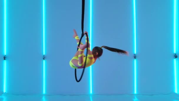 Nuori antenni voimistelu suorittaa akrobaattisia temppuja ilmassa vanne. Jännittävä akrobaattinen show suoritetaan teini tyttö taustaa vasten kirkkaita neon valot. Hidastus. — kuvapankkivideo