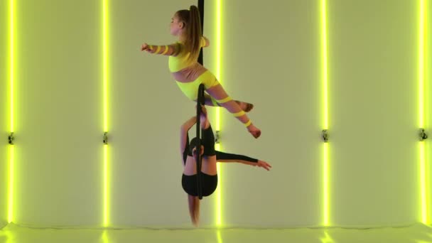 Zwei junge Zirkusartisten drehen sich an einem Luftkorb. Mädchen in gelben und schwarzen Trikots zeigen akrobatische Stunts in der Höhe. Gedreht im Studio mit hellen Neonlichtern im Hintergrund. Zeitlupe. — Stockvideo