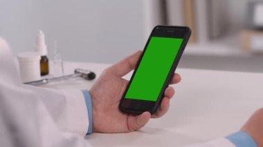 Male doctor consults patient using mobile phone with green screen chroma key. Online remote distance examination diagnosis by video call conference chat. Telemedicine. Close up. Slow motion.