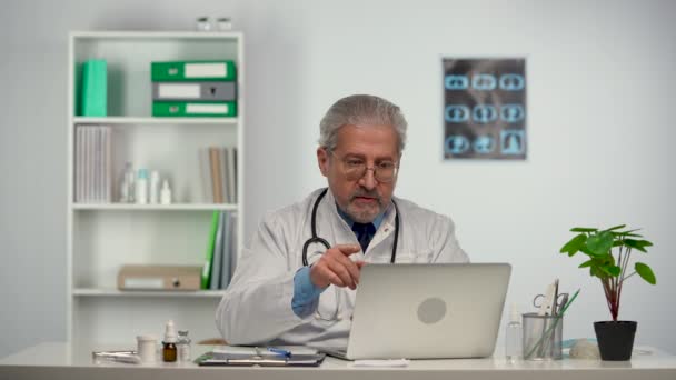 Professional male doctor in white medical coat making conference call on laptop computer, consulting distance patient online in video chat, explain treatment by webcam concept. Slow motion. — Vídeos de Stock