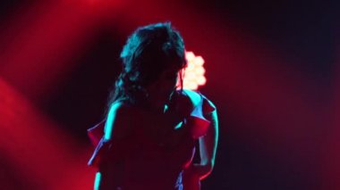 Uzun kırmızı elbiseli tutkulu esmer, koyu renkli bir stüdyoda ateşli bir flamenko dansı yapıyor. İspanyol bayan dansçı hareketlerini kapat. Siluet.