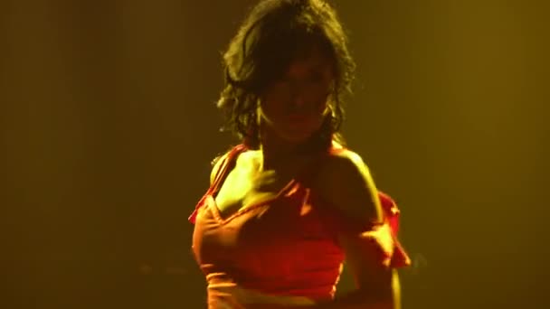 Brunette in long red dress dancing passionate flamenco dance against background of yellow neon lights in dark smoky studio. Close up argentinian female dancer whirls dancing. Silhouette. — Stock Video