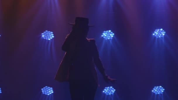 Silhuett av attraktiv kvinna i byxdräkt och hatt, utför en argentinsk flamenco dans koreografi i mörkret mitt i blå studiobelysning. Spanska dansare rör sig elegant i slow motion. Närbild — Stockvideo