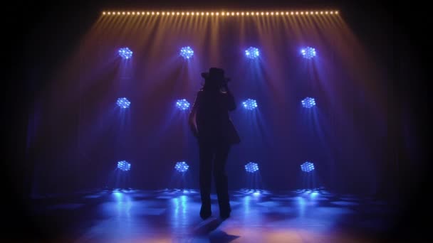 Silhouette of attractive woman in pantsuit and hat, performing an Argentinean flamenco dance choreography in the dark amidst blue studio lights. Spanish dancer moves elegantly in slow motion. — Stock Video