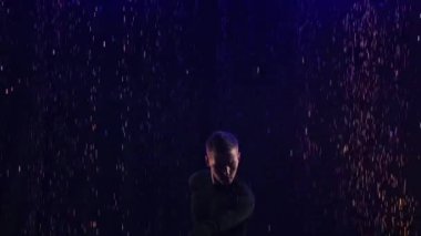 Balo dansçısı erkek dansçı yağmurda ve su sıçratma yarışmasında Latince dans figürleri sergiliyor. Bir adam, karanlık bir stüdyoda suyun yüzeyinde mavi ışıkla dans ediyor. Ağır çekim. Kapat..