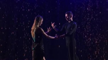 Genç ve şehvetli dansçıların yaptığı yağmur damlaları arasında tutkulu bir bachata dansı. Ortaklar, mavi neon ışıklar arasında siyah bir stüdyoda dans ediyorlar. Kapatın. Yavaş çekim.