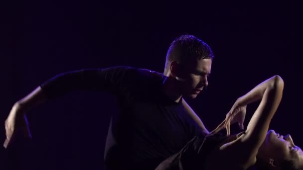 Bachata apaixonado dança entre as gotas de chuva realizadas por um jovem casal sensual de dançarinos. Os parceiros se movem em uma dança em um fundo de estúdio preto entre as luzes de néon azul. Fecha. Movimento lento. — Vídeo de Stock