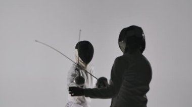 Turnuvada dövüşen iki kadın eskrimcinin arkasındaki manzara. Antrenman, spor, antrenman. Gri bir arka planda düellocu karanlık siluetleri. Kapatın. Yavaş çekim.