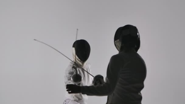 Вид позаду двох жінок-фехтувальниць, що воюють на турнірі. Практика, спорт, тренування. Темні силуети дуелістів на сірому студійному фоні. Близько. Повільний рух . — стокове відео