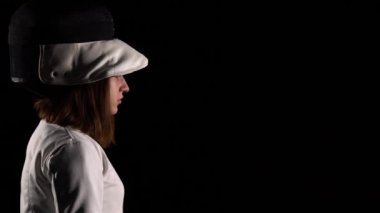 Genç kadın eskrimci, koruyucu spor maskesi kaskı takıyor. Beyaz üniformalı bir bayan atlet siyah stüdyo geçmişinde Rapier ile poz veriyor. Eskrim okulu posteri. Kapat..