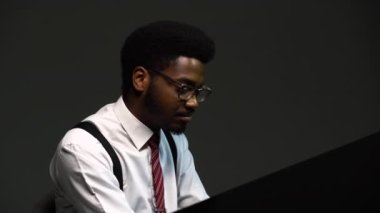Yakışıklı, şık takım elbiseli, gözlüklü Afro-Amerikan bir adam büyük piyanoda zevkle şarkı söyler ve besteler. Siyah bir sanatçı stüdyoda gri bir arkaplanda gösteri yapıyor. Kapat..