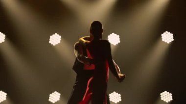 Bir çift balo dansçısı tarafından yapılan tutkulu bir tango dansı. Karanlık bir stüdyoda parlak ışıklarla Latin dansı yapan şık bir kadın ve erkek. Siluetler. Kapat..