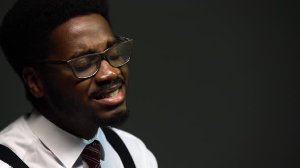 Bello uomo afroamericano in un abito elegante e bicchieri canta con piacere, chiudendo gli occhi. Un performer nero si esibisce su uno sfondo grigio nello studio. Da vicino.. — Video Stock