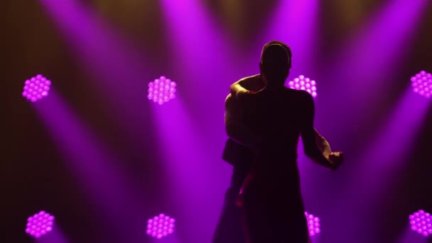 Passionate young couple dancing classic Argentine tango in a dark studio with bright purple lights. Woman in red dress and man in stylish suit perform dance show at the holiday. Silhouettes. Close up. — Stock Video