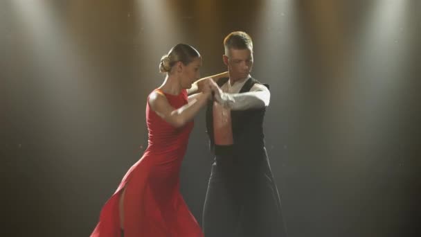 Een gepassioneerde tango dans uitgevoerd door een paar ballroom dansers. Stijlvolle man en vrouw die latijnse danselementen dansen in een donkere studio met felle lichtjes. Sluiten.. — Stockvideo