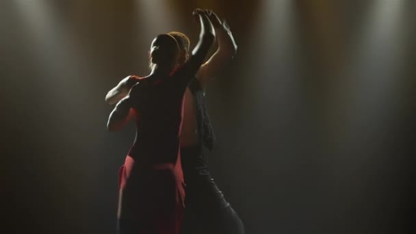 Een gepassioneerde tango dans uitgevoerd door een paar ballroom dansers. Stijlvolle man en vrouw die latijnse danselementen dansen in een donkere studio met felle lichtjes. Silhouetten. Sluiten.. — Stockvideo