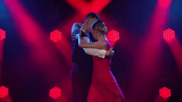 Půvabné argentinské tango mezi kouřem a jasně červenými neonovými světly v tmavém studiu. Taneční show v podání vášnivých tanečních partnerů. Zavřít. — Stock video