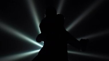 Dans eden çiftlerin siyah siluetleri Arjantin tangosu icra ediyor. Tutkulu çift, parlak ışıklar saçan karanlık bir stüdyonun arka planında ağır çekimde hareket ediyor. Kapat..