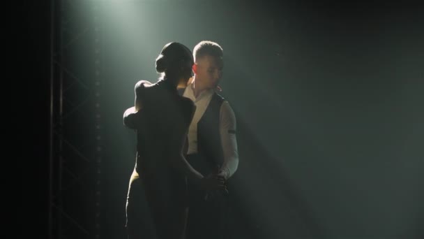 Emotionele uitvoering Argentijnse tango door professionele ballroom dansers. Man en vrouw dansen met plezier hand in hand in donkere rokerige studio met felle spots. Silhouetten. Sluiten.. — Stockvideo