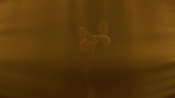 Vor dem rauchgelben Hintergrund des dunklen Studios erscheinen Silhouetten eines Tanzpaares, das Elemente des argentinischen Tanzes vorführt. Nahaufnahme. — Stockvideo