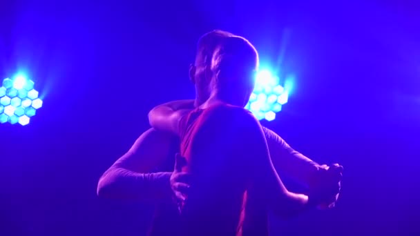 Um par de artistas de tango dançam juntos, rodopiando e segurando as mãos apaixonadamente em um estúdio escuro com luzes azuis brilhantes. Silhuetas de figuras esbeltas. Fecha. Movimento lento. — Vídeo de Stock