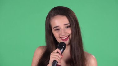 Güzel genç bir kadının portresi kameraya bakıp mikrofona şarkı söylüyor. Uzun saçlı, kırmızı elbiseli, stüdyoda yeşil ekranda poz veren bir model. Ağır çekim. Kapat..