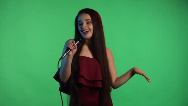 Retrato de una hermosa joven iluminada por luz azul de neón canta canción en el micrófono. Modelo con pelo largo en vestido rojo posando en pantalla verde en el estudio. En cámara lenta. De cerca.. — Vídeo de stock