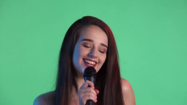 Portrét mladé ženy ozářený modrým červeným neonovým světlem zpívá píseň do mikrofonu a tančí na hudbu. Model s dlouhými vlasy v červených šatech pózuje na zelené obrazovce ve studiu. Zpomal. Zavřít. — Stock video