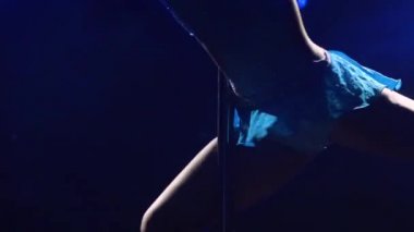 Atletik esnek bir kadın, karanlık bir stüdyoda mavi ışıklı bir direğin üzerinde döner. Dans eden koreografi elementleri, aerobik, fitness. Kapatın. Yavaş çekim.