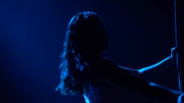 Sıska, genç, atletik bir kadın karanlık dumanlı bir stüdyoda vücudunun esnekliğini gösteriyor. Mavi bir ışık hüzmesi seksi bir jimnastikçinin siluetini aydınlatır. Kapatın. Yavaş çekim