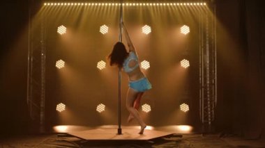 Mavi taytlı esnek bir kadın tarafından sahnelenen akrobatik unsurlarla dolu bir direk dansı. Karanlık bir stüdyoda duman ve ışıklarla spor yapmak. Yavaş çekim.