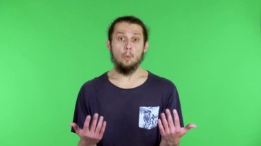 Kameraya bakan genç bir adamın portresi, ellerini öfkeyle sallıyor, ellerini şakaklarına koyuyor, bu şekilde. Stüdyoda yeşil ekranda poz veren siyah saçlı adam. Kapat..