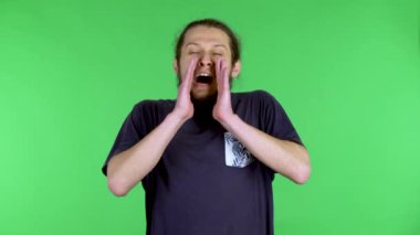 Adam ellerini ağzına koydu ve yüksek sesle ve mutlu bir şekilde bağırdı. Fan veya ponpon kız. Stüdyodaki sakallı, siyah saçlı adam yeşil ekranda. Kapat..