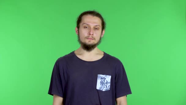 Retrato de un joven mirando a la cámara, cansado y suspirando. Hombre de pelo oscuro barbudo posando en el estudio en una pantalla verde. De cerca.. — Vídeo de stock